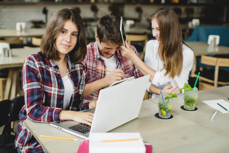 Kobieta przy laptopie siedząca obok śmiejącej się pary